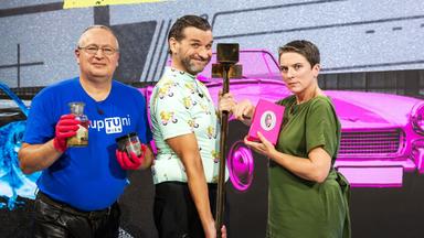 Das Bild zeigt drei Personen, die nebeneinander stehen. Im Hintergrund ist ein grafisches Muster mit der Aufschrift "IHR HABT WOHL DIE TECHNOLOGIE OFFEN" in gelben Buchstaben auf einem dunkelgrauen Untergrund. Die erste Person links trägt ein blaues T-Shirt mit der Aufschrift "upTuni Wien" und hält eine Glasflasche sowie ein schwarzes Behältnis in den Händen. Sie hat eine Brille auf und trägt rote Handschuhe.   In der Mitte steht eine zweite Person in einem hellen Hemd mit einem bunten Muster aus kleinen Figuren. Diese Person hat eine verspielte Miene und hält einen langen Stock.   Die dritte Person auf der rechten Seite trägt ein grünes Oberteil und sieht ernst aus. Sie hält ein pinkes Notizbuch oder ein ähnliches Objekt in der Hand und hat eine kurze Frisur. Im Hintergrund sind farbenfrohe grafische Elemente, darunter ein pinkes Auto und eine cartoonartige Illustration eines Tieres. Die gesamte Szenerie hat einen modernen und dynamischen Charakter.