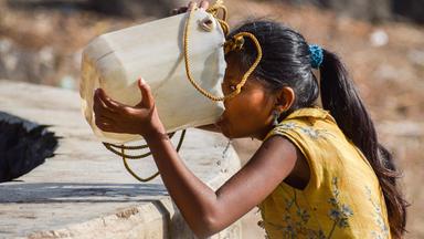 Ein Mädchen trinkt Wasser aus einem Plasitkkanister.