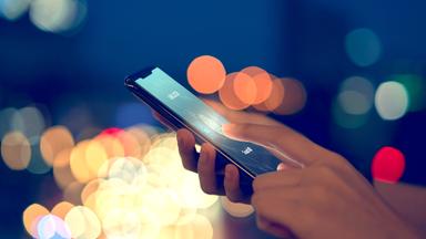 Eine Frau hält ihren Finger auf das Touchfeld ihres Smartphones, um es zu entsperren.