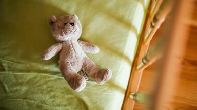 Ein Teddybär liegt im Kinderbett.