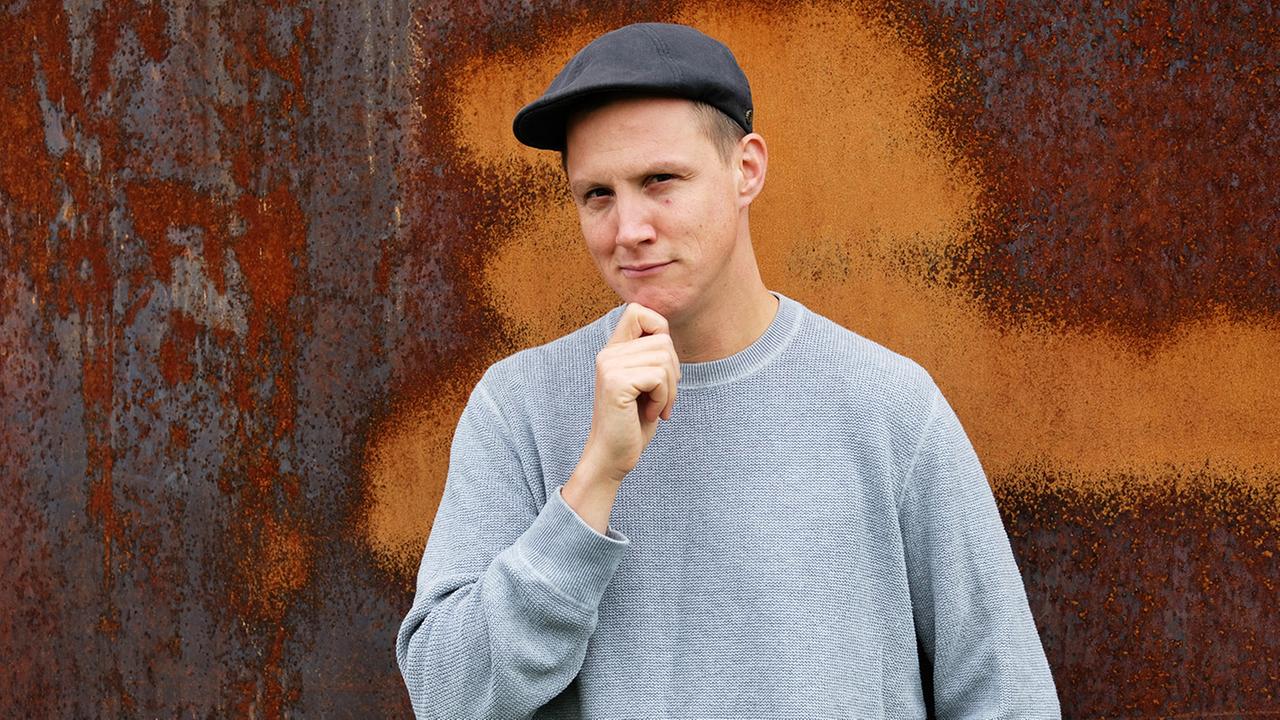 Junger Mann mit Baseballkappe und Pullover posiert für ein Porträtbild.