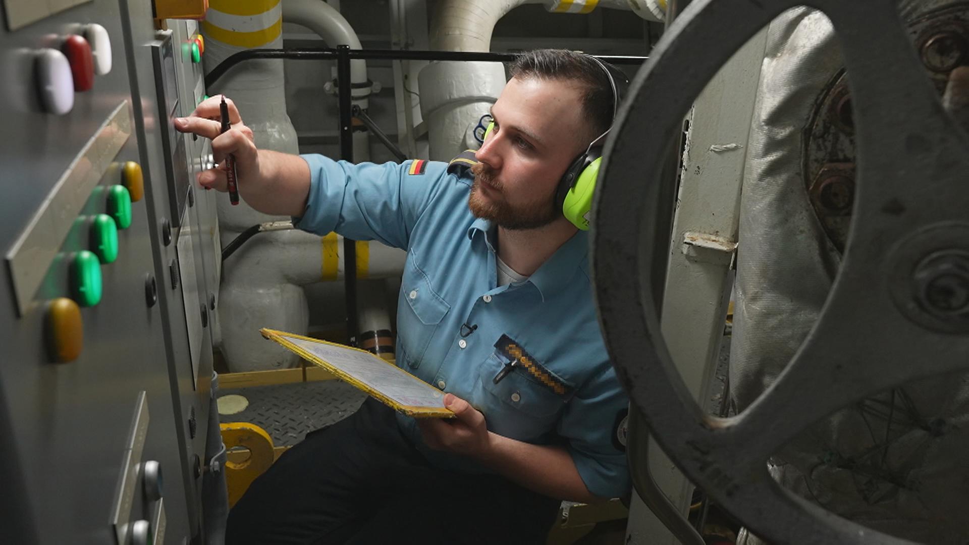 Robin, in Uniform, kniet vor technischen Geräten.