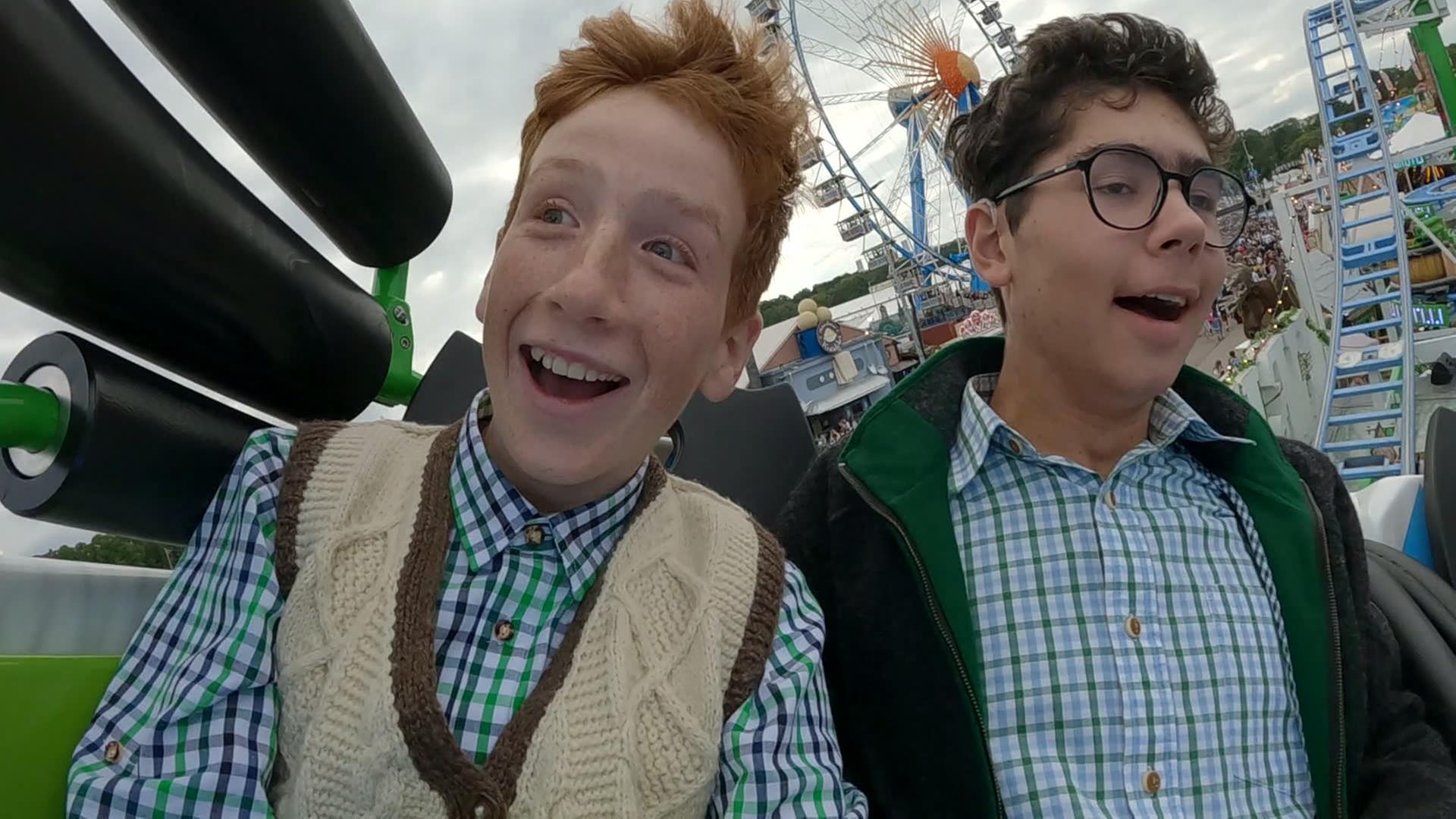 Zwei Jungen in karierten Hemden und Trachtenweste lachen fröhlich auf dem Oktoberfest.