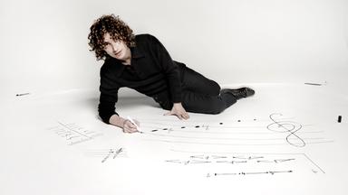 Ein junger Mann liegt auf einem weißen Boden und schreibt mit Edding Noten.