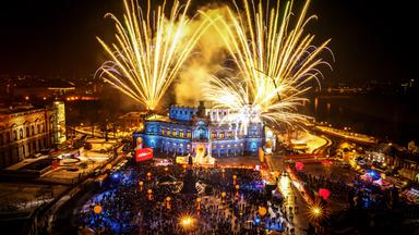 Blick auf die Semperoper und Umgebung von außen. Zu sehen ist ein großes Feuerwerk und reges Treiben auf dem Vorplatz.