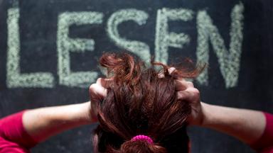 Eine Frau ist von hinten zu sehe, rauft sich die Haare beim Blick auf eine Tafel, auf der das Wort LESEN steht.