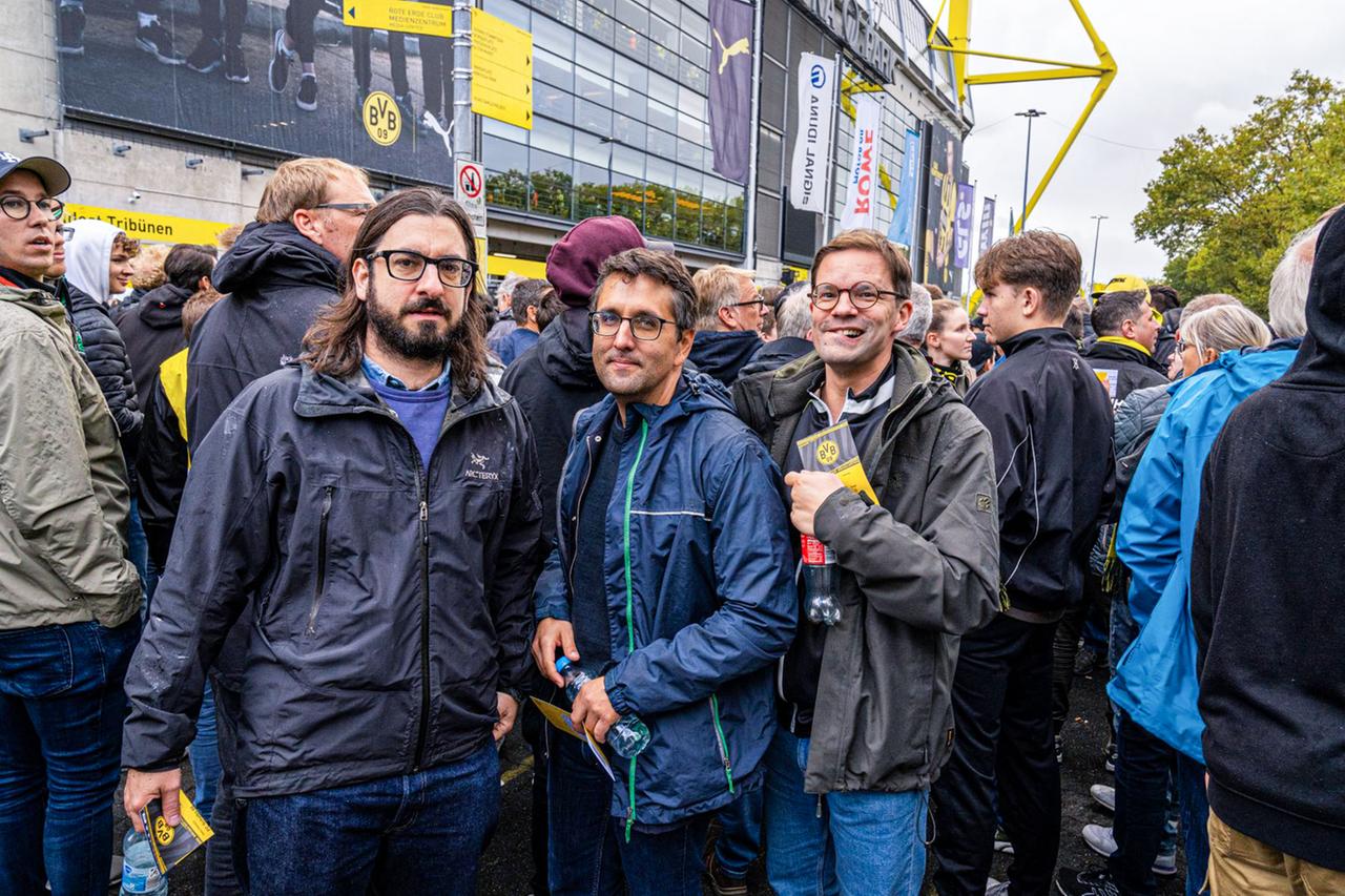 Drei Männer in einer Menschenmenge vor dem Stadion