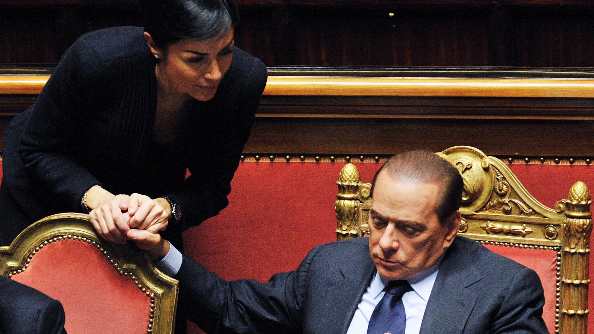 Silvio Berlusconi hält mit einer Frau die Hand.