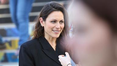 Eine Frau mit langen Haaren und dunklem Jacket lächelt.