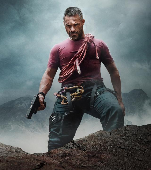 aul Vilar (Philippe Bas) steht auf einem Felsen und schaut in die Tiefe. Er hält eine Pistole in der Hand.
