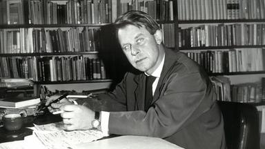  Der junge Siegfried Lenz sitzt vor einer Bücherwand am Schreibtisch (s/w). 