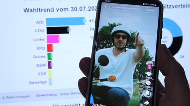 Eine Hand hält ein Smartphone, auf dem eine TikTok-Seite zu sehen ist, die einen Mann mit Helm und Sonnenbrille auf einem Moped zeigt.