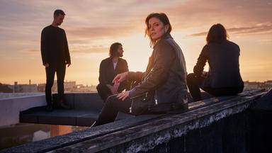 Die vier Bandmitglieder von Silbermond sitzen auf einem Dach, die Sonne geht unter.