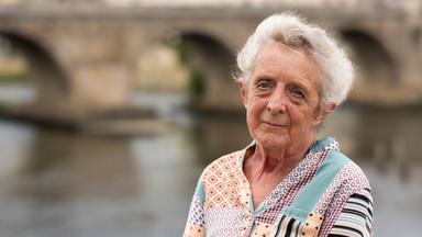 Porträtfoto einer älteren Frau mit grauen Haaren und bunter Bluse.