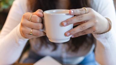 Frau hält eine Kaffeetasse in beiden Händen 