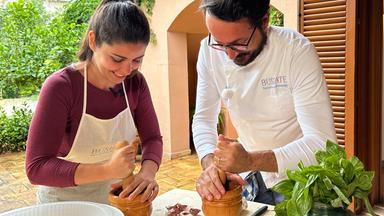 Eine Frau und ein Mann zerkleinern Knoblauch in zwei Mörsern. 