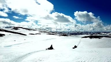 "Skandinaviens versteckte Paradiese": Totale: Zwei Schneemobile fahren über weite Schneeflächen, Himmel dunkelblau mit weißen Wolken.