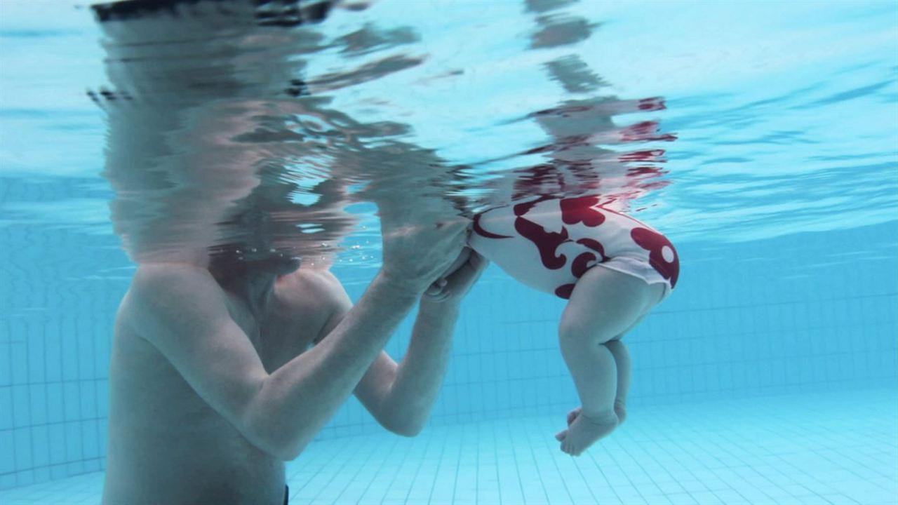 Ein Mann und ein Baby schwimmen. Dabei sind ihre Köpfe nicht zu sehen, da das Foto unter Wasser aufgenommen wurde.