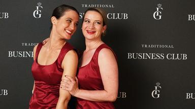 Kim (Friederike Becht) und Maja (Nina Gummich), in roten Cocktailkleidern, stehen lachend vor einer Fotowand eines Events.