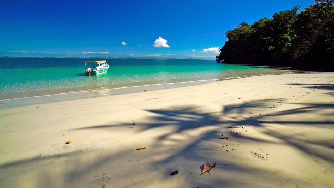 Vor einem Sandstrand mit türkisem Meerwasser schwimmt ein Boot