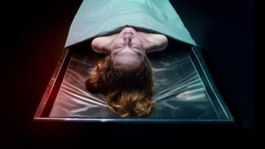 Die Leiche einer Frau liegt auf einem Obduktionstisch. Ihr Kopf und die Schulterpartie ragen unter einem Tuch hervor.