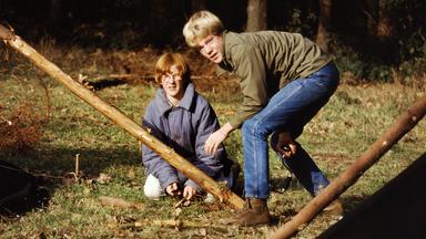 Zwei Jugendliche mit großen Holzpfahlen auf einer Wiese