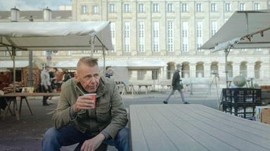 Ein Mann mit Pappbecher auf einem Stuhl.