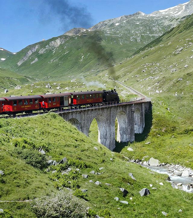 Zug fährt durch eine Berglandschaft über ein Aquaduct