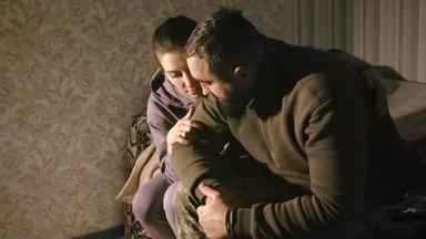 Ein Mann und eine Frau sitzen eng umschlungen auf einem Bett.