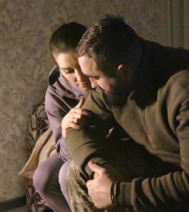 Ein Mann und eine Frau sitzen eng umschlungen auf einem Bett.