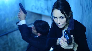 June (Tuppence Middleton) und Ed Lansbury (Ronan Summers) laufen mit gezückten Revolver die Treppen hoch, sichern sich nach allen Seiten ab, June schaut nach vorne, Ed nach oben.