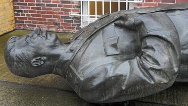 Eine Männrestatue liegt auf dem Rücken in einem Hof.