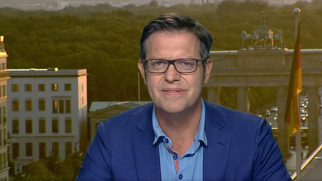 Ein Mann mit Brille und blauem Anzug vor dem Hintergrund des Brandenburger Tors in Berlin