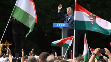 Der ungarische Premierminister Viktor Orbán spricht während eines Antikriegs-Friedensmarsches in Budapest. Er winkt vielen, den vor ihm versammelten Menschen, zu, die teilweise die ungarishe Flagge schwenken.