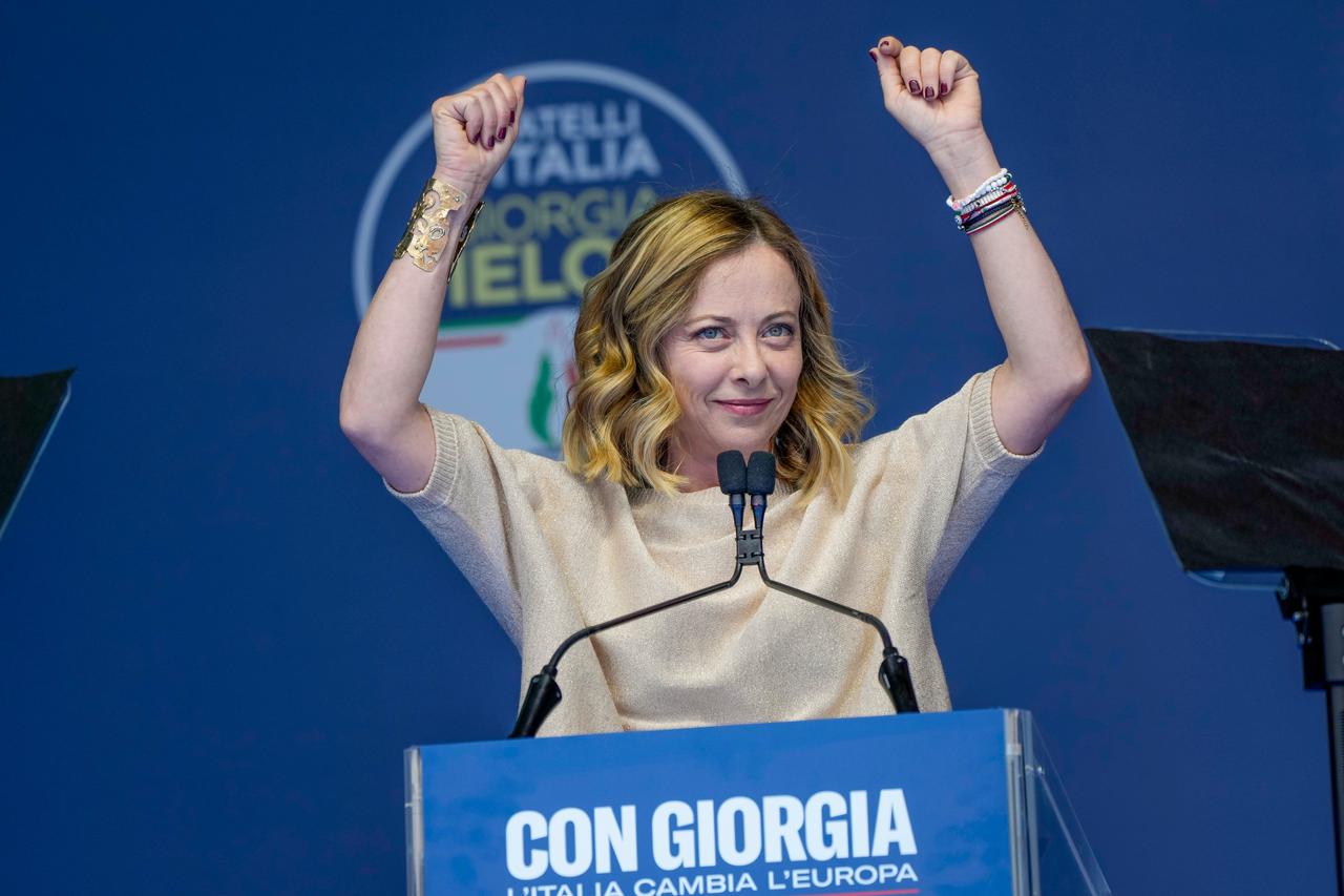 Die italienische Ministerpräsidentin Giorgia Meloni hebt bei einer Rede beide Arme in die Luft und lächelt.