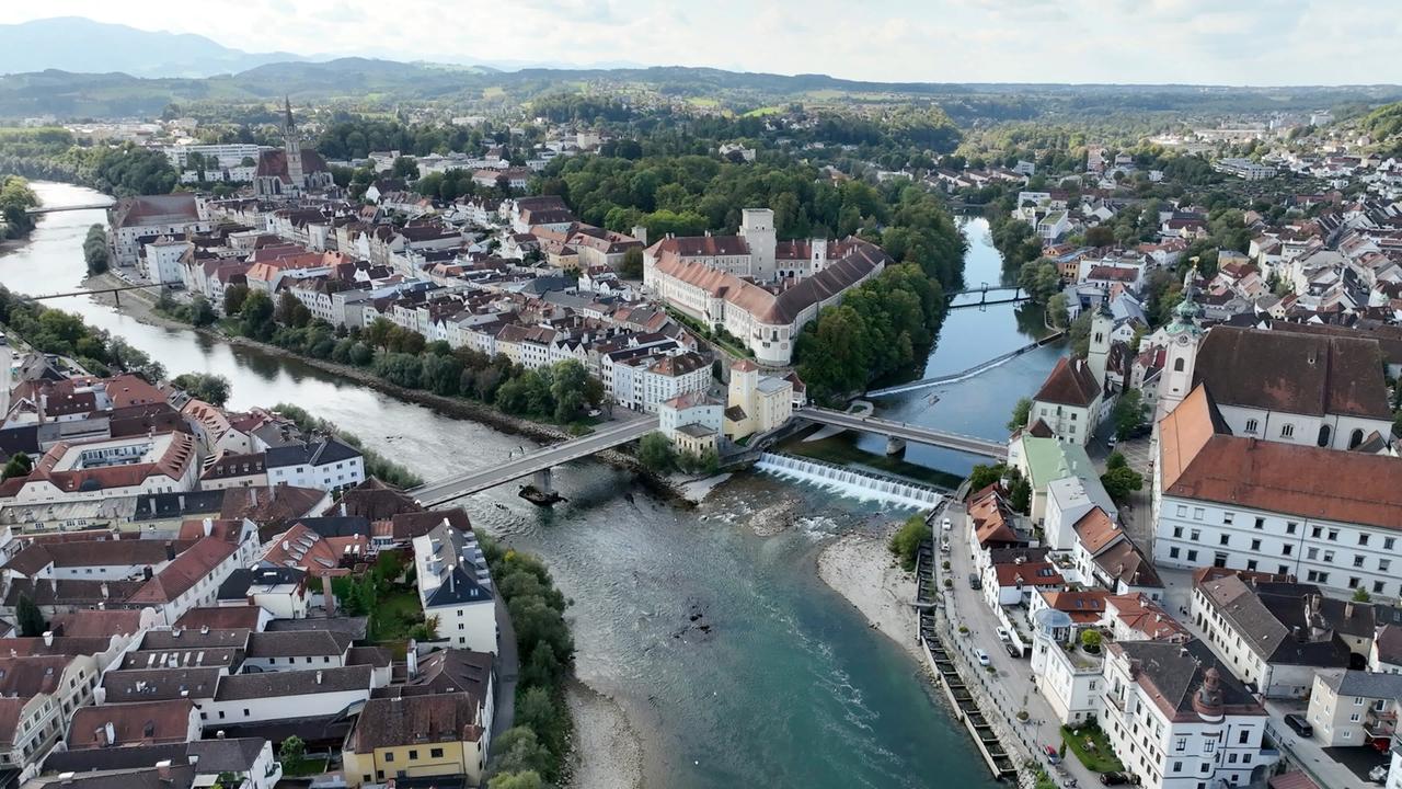 Luftaufnahme des Zusammenflusses von Steyr und Enns in Steyr, Oberösterreich, mit historischer Altstadt, Schloss Lamberg und umliegender Hügellandschaft.