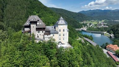 Luftaufnahme von Schloss Klaus im Steyrtal, Oberösterreich, gelegen am bewaldeten Hang über der Steyr mit Blick auf den Fluss und umliegende Berge.