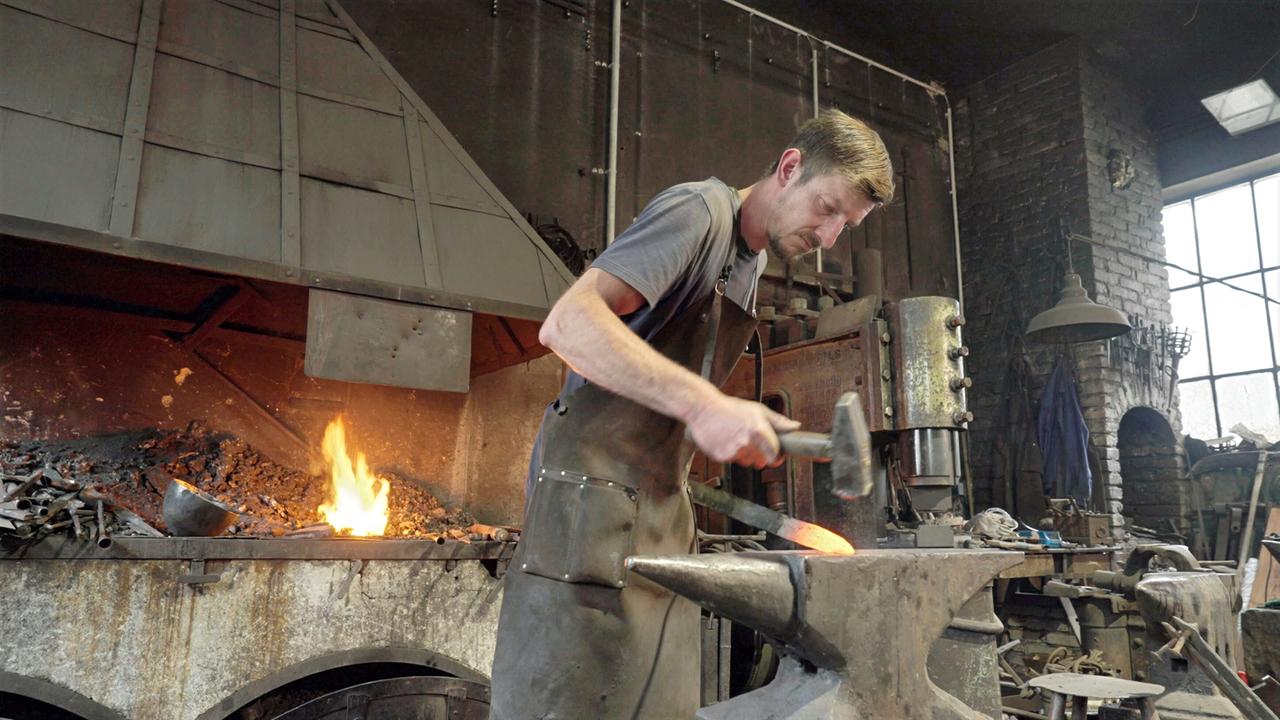 Schmied bei der Arbeit in einer traditionellen Werkstatt mit Amboss, Hammer und Schmiedefeuer.