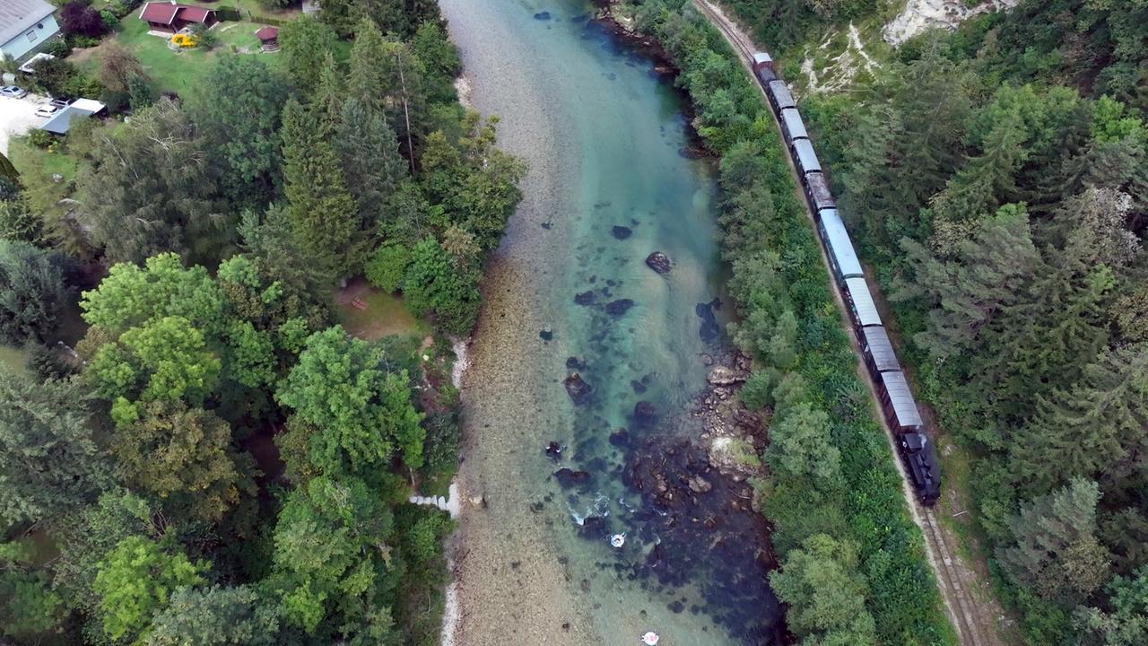 Luftaufnahme der Steyrtalbahn, die entlang des klaren Flusses Steyr durch bewaldete Landschaft in Oberösterreich fährt.