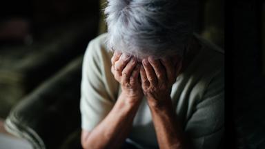 Eine Seniorin hält sich die Hände vors Gesicht.