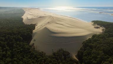 Die gewaltige Dune du Pilat mit Sandmassen, umgeben von Wald und Meer im Hintergrund.