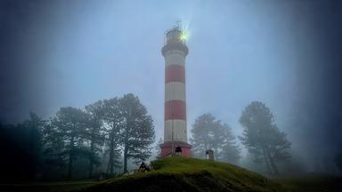 Der Leuchtturm von Nida an einem nebligen Abend mit beleuchteter Spitze.