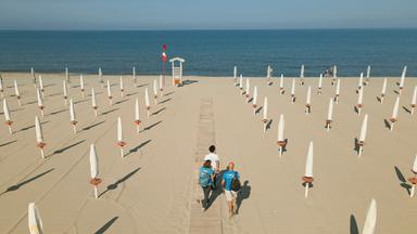 Strandszene mit akribisch angeordneten Sonnenschirmen und drei Menschen auf einem Holzweg.