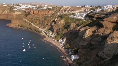 Küstenlandschaft mit schwarzem Sandstrand an der Innenseite eines Vulkankraters auf Santorin.