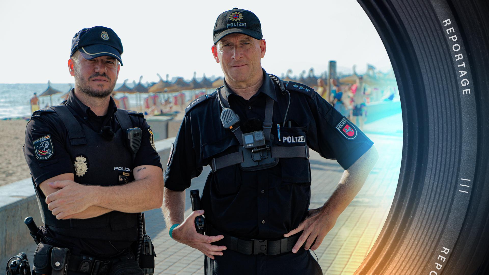 Zwei Polizisten, Javier Pulpillo-Mas und Torsten Obst, stehen an der Strandpromenade von Palma de Mallorca. Im Hintergrund liegt das Meer und der Strand, an dem sich Badende befinden.