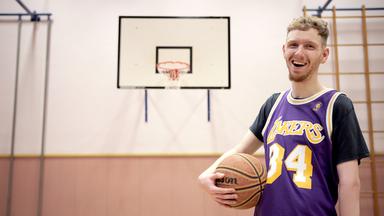 Simon in einer Sporthalle mit Basketball in der Hand.