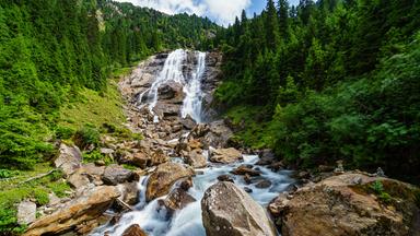 Zwischen Tannenwäldern verläuft der Wasserfall vor strahlend blauem Himmel