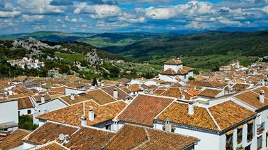 Blick über die weißen Häuser und roten Ziegeldächer von Grazalema in Andalusien. Im Hintergrund erstreckt sich eine grüne, bergige Landschaft.