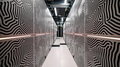 Blick in einen langen engen Gang zwischen zwei Reihen von Metalltüren, die mit einem schwarz-weißen Wellenmuster dekoriert sind.