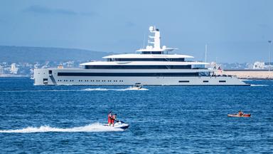 Eine Superjacht auf dem Meer, im Vordergrund sind kleine Boote mit Menschen zu sehen.